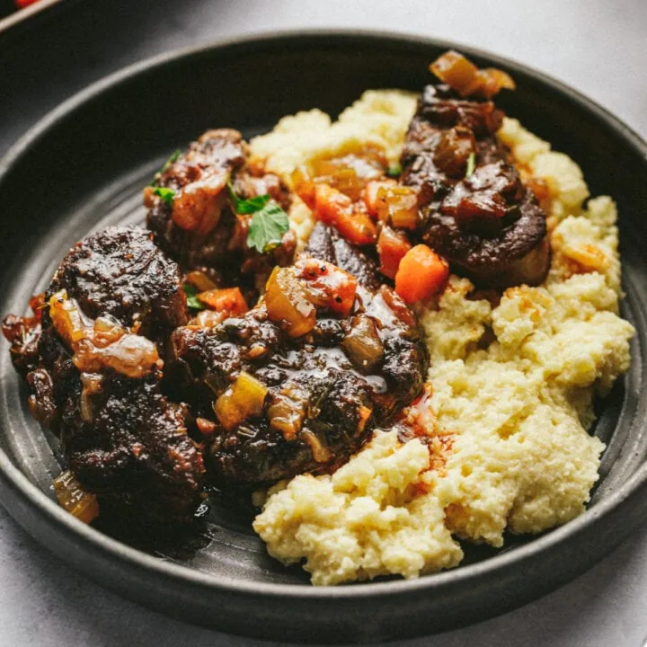 A plate with braised beef shanks and carrots over cauliflower mash.