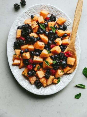 A platter of keto fruit salad with a wooden serving spoon.