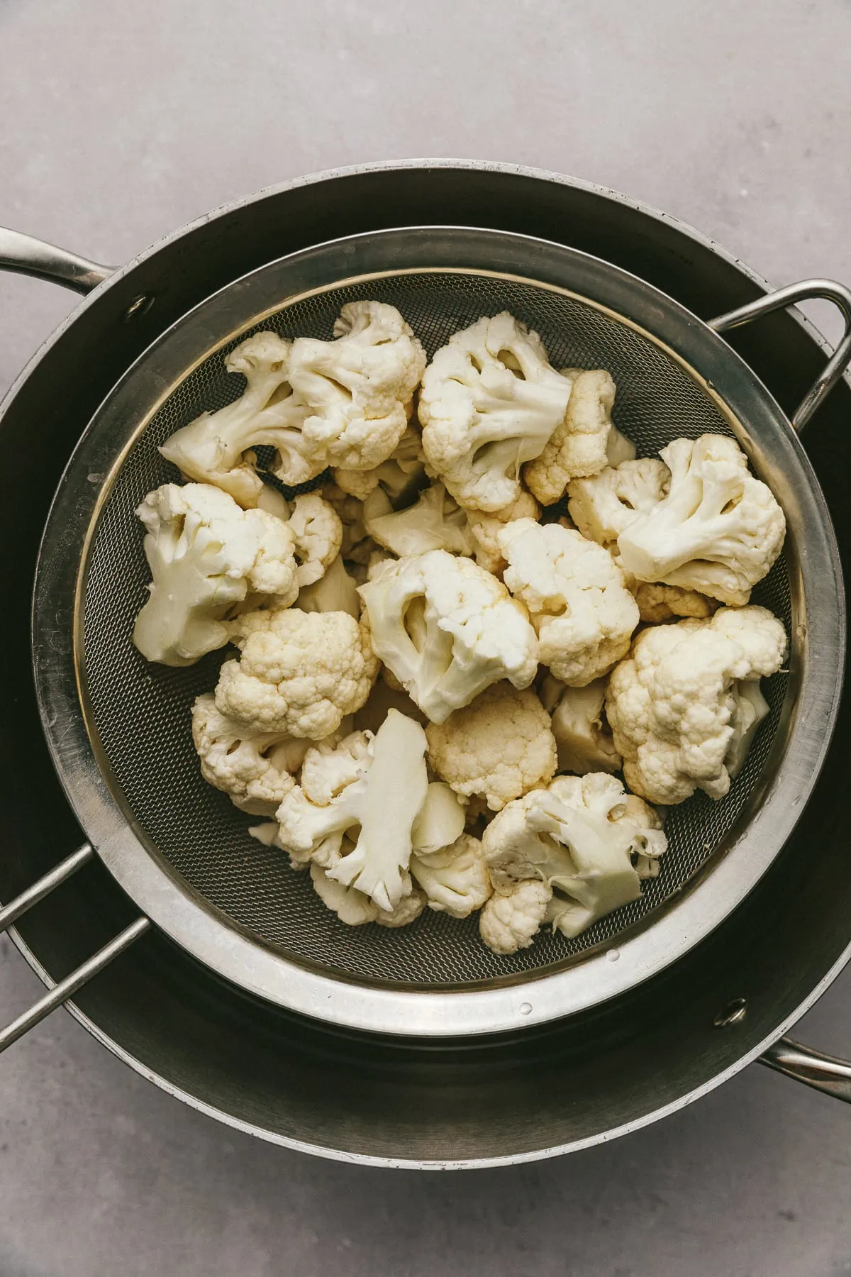 Cauliflower florets in a mesh strainer over a pot of boiling water. 