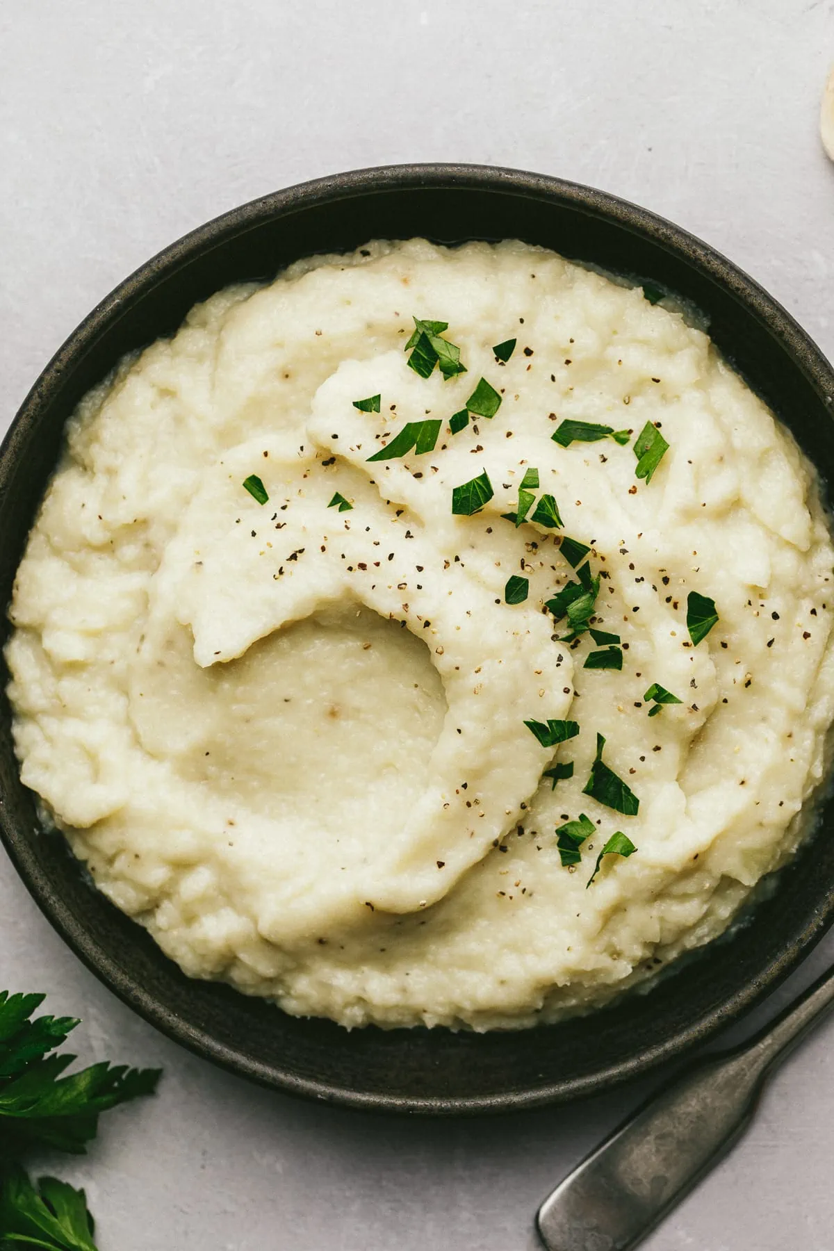 Overhead shot of keto and dairy-free mashed cauliflower in a black serving dish with chopped parsley.