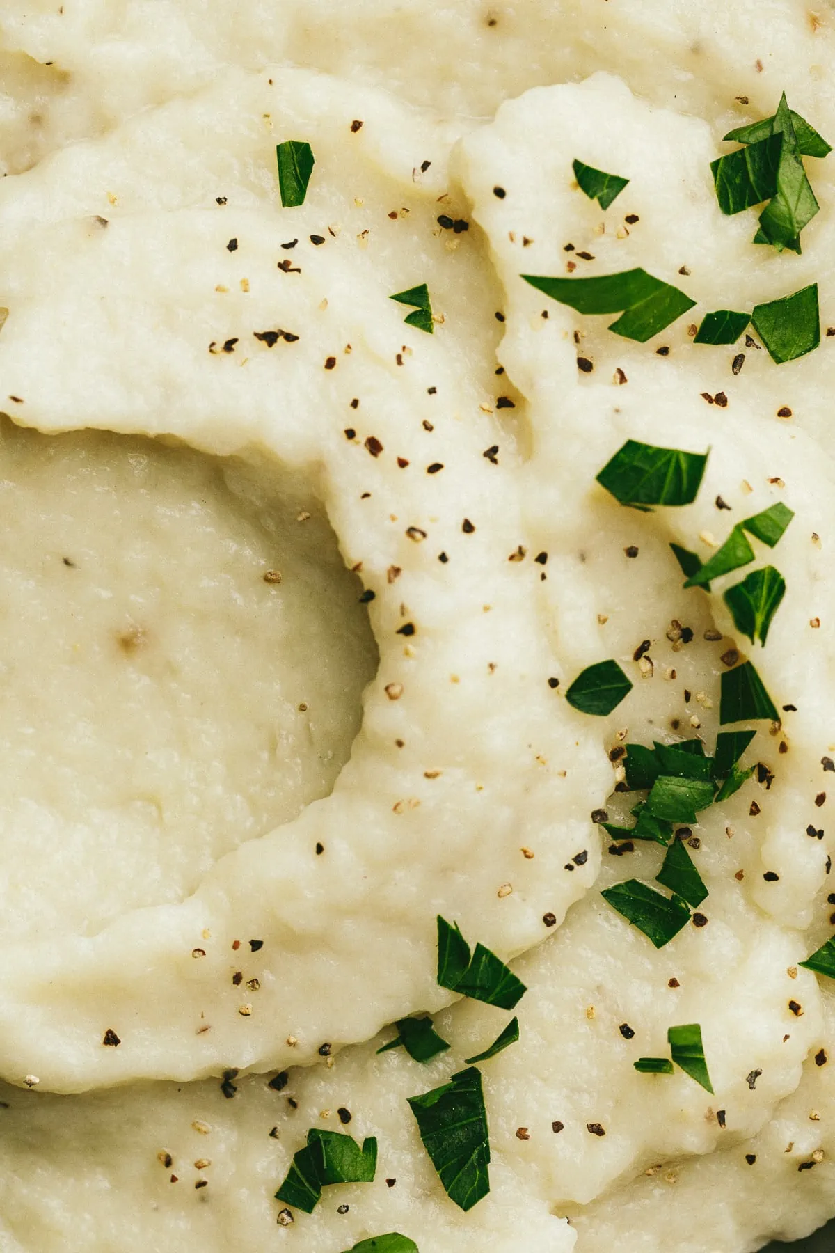 Closeup of chopped parsley and pepper on a bowl of dairy-free cauliflower mash.