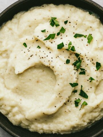 Dairy-free mashed cauliflower in a black dish with garnishes.