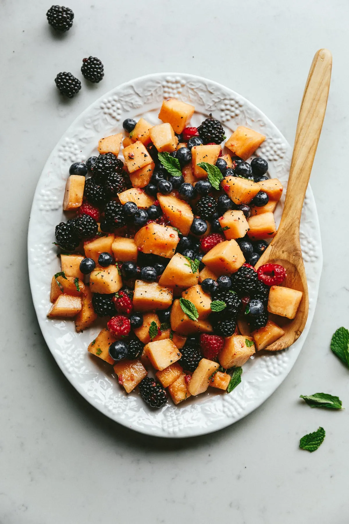 A platter of keto fruit salad with a wooden serving spoon.