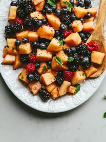 Low carb fruit salad on a serving plate with a wooden spoon.