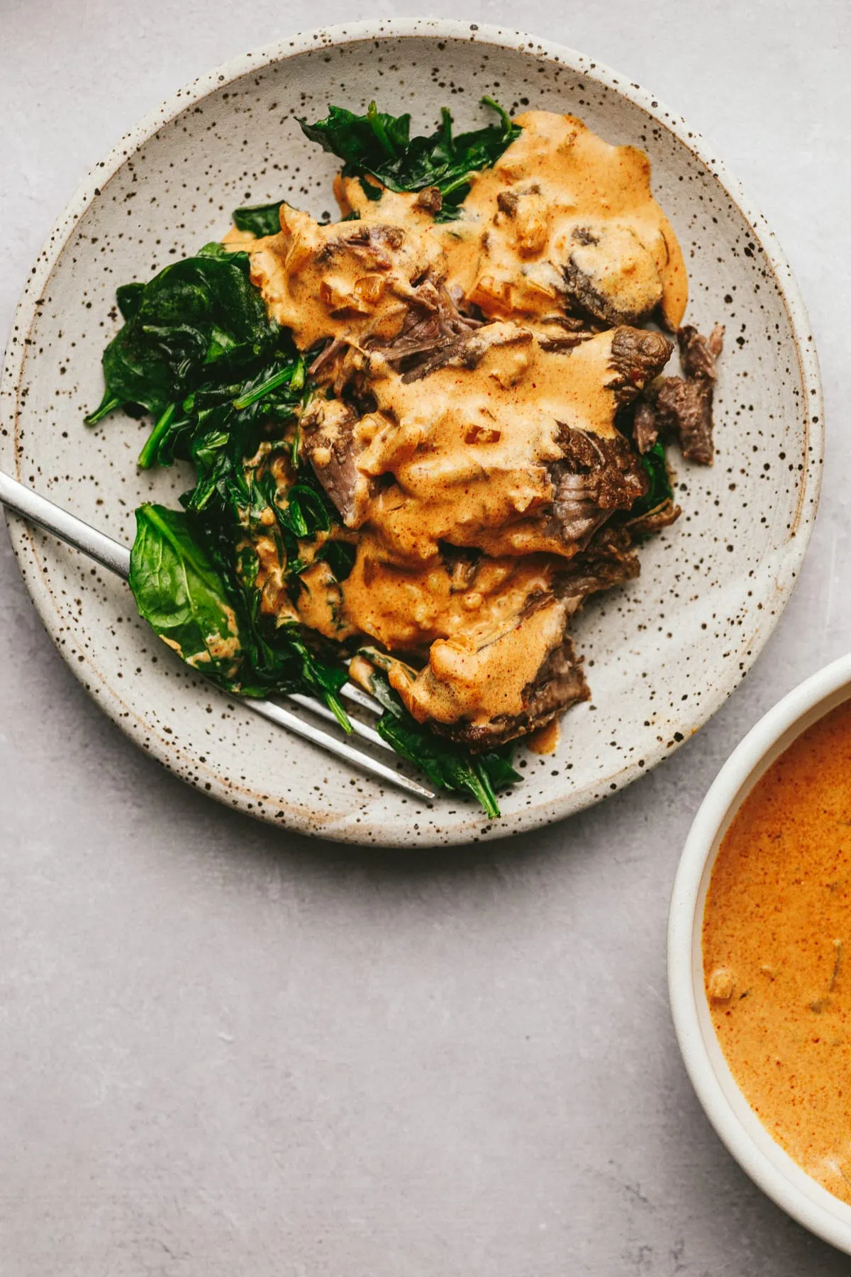 Paprika sauce on top of beef and spinach with a bowl of it on the side.