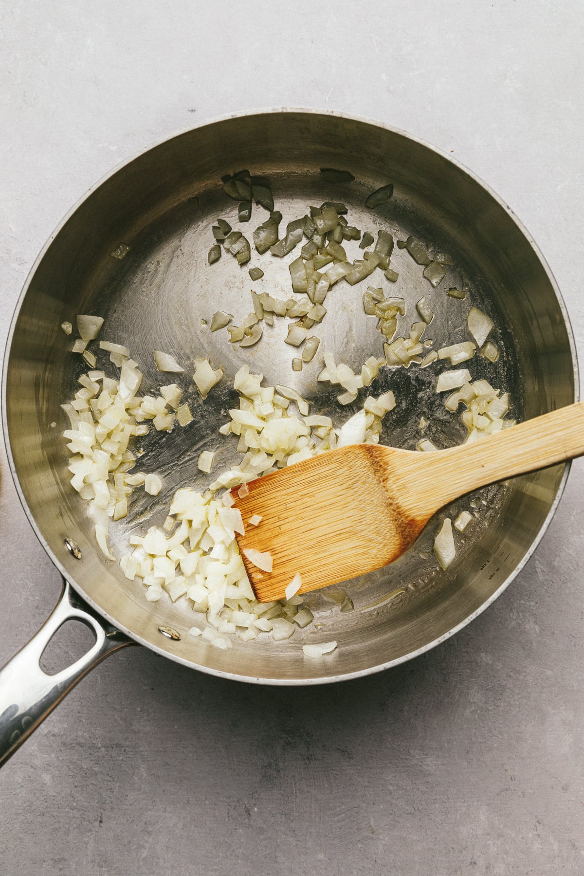 Onions in a stainless steel skillet with a wooden spatula.