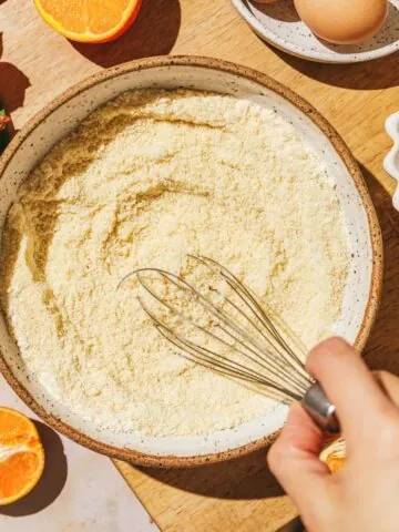 Almond flour in a bowl with a whisk and ingredients around it.