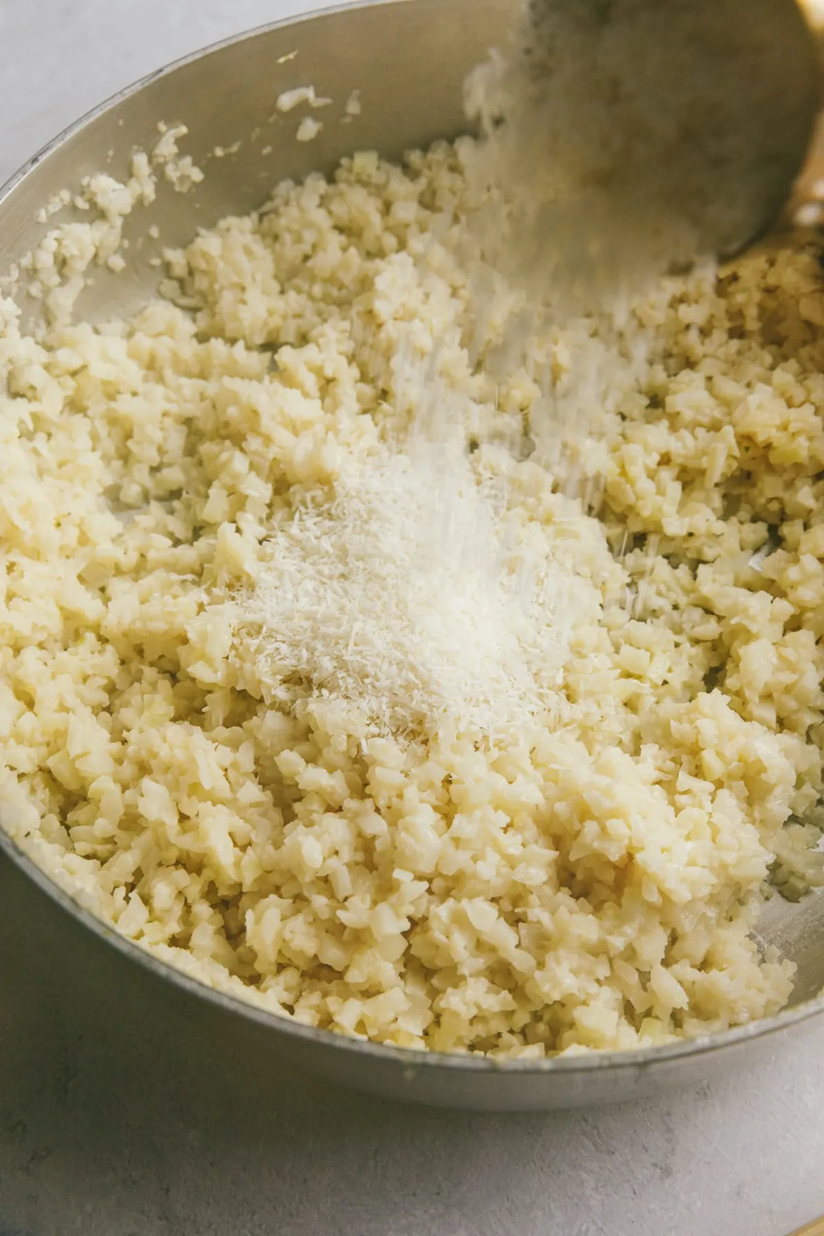 Pouring coconut flakes into cauliflower rice in a skillet.
