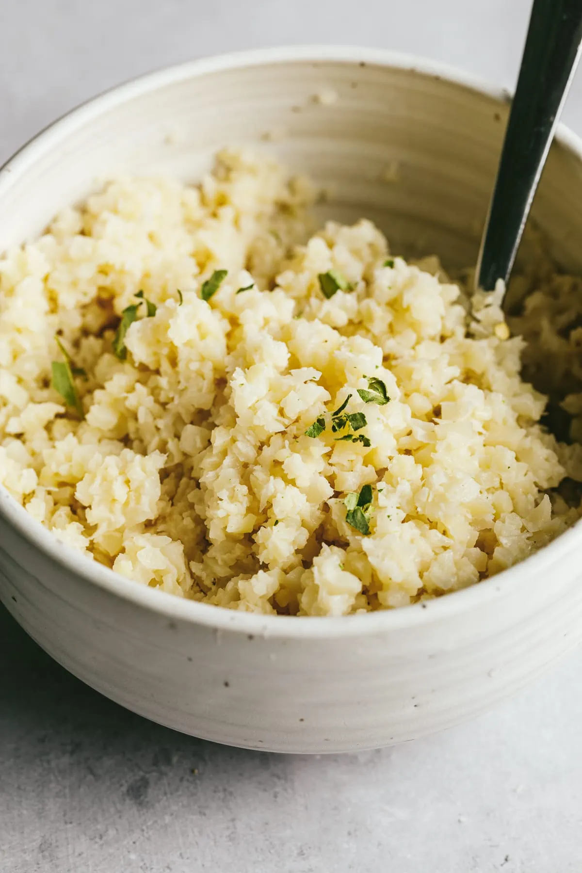 Closeup of coconut cauliflower rice in a white serving bowl with kaffir lime leaves crushed on top.