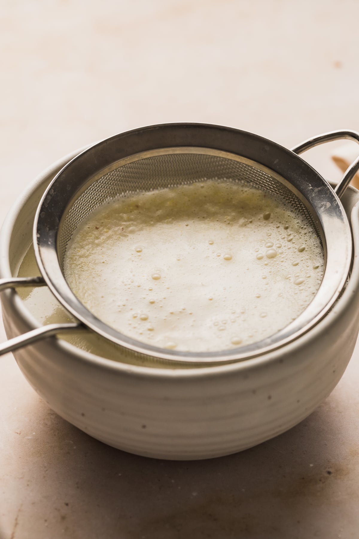 Straining the pulp with a fine mesh strainer over a white bowl.