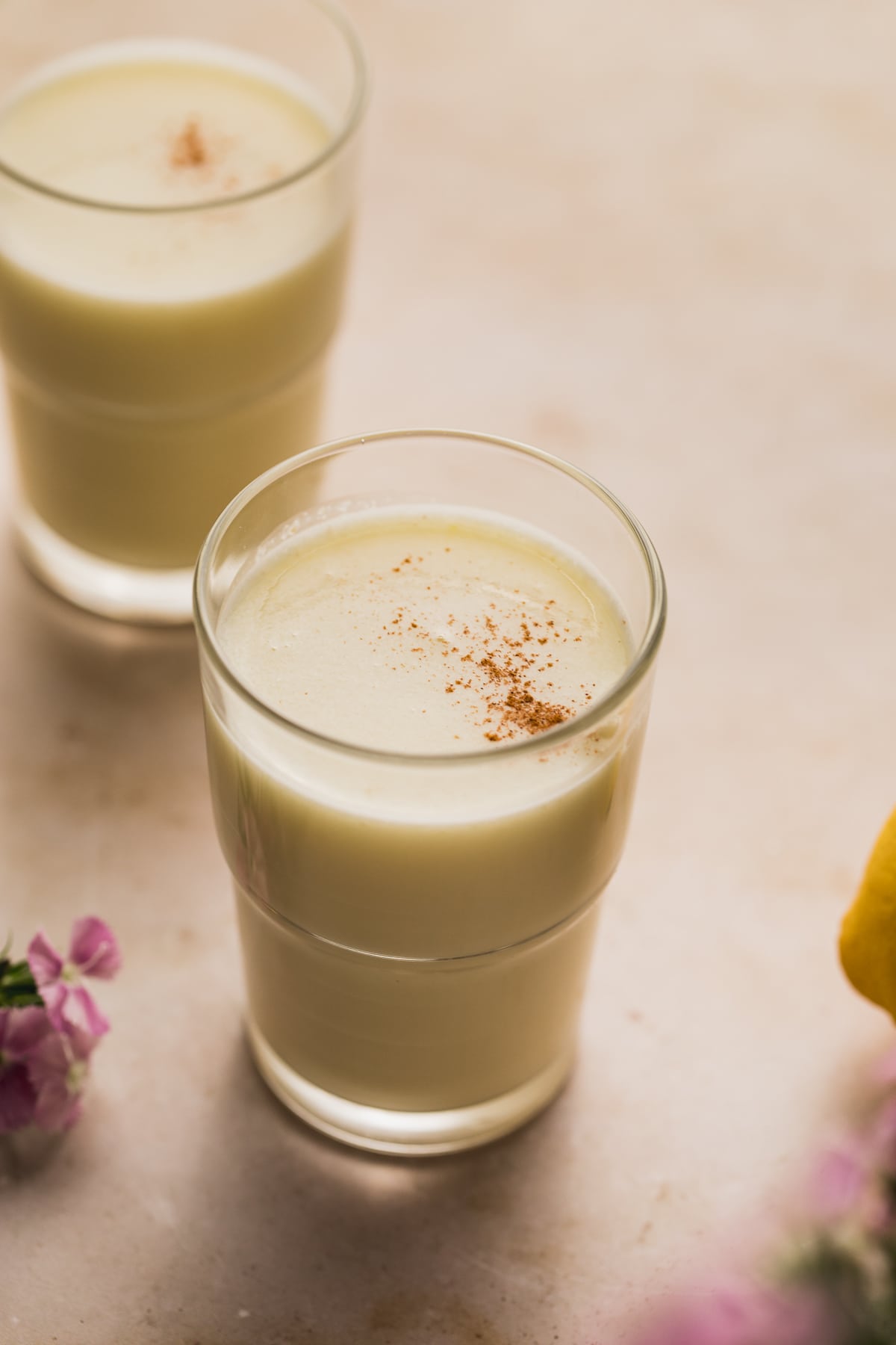 A glass of lemon juice with purple flowers next to it.