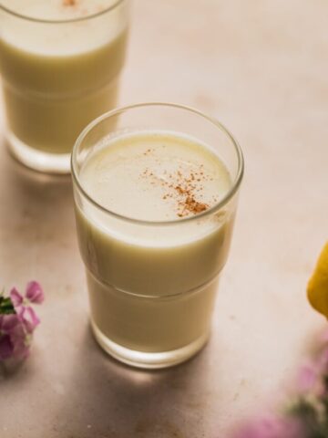 A glass of lemon juice with purple flowers next to it.
