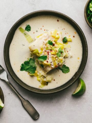 A black bowl with a piece of cod and coconut milk with leeks.