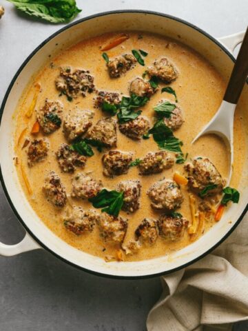 Overhead image of keto turkey meatballs in red curry sauce with a serving spoon.