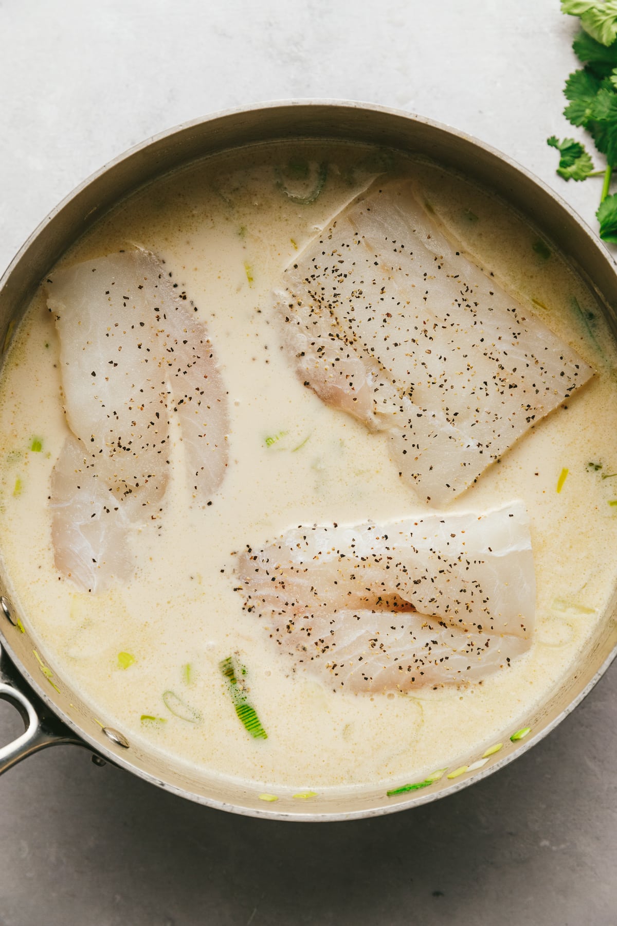 Cod poaching in coconut milk in a pan.