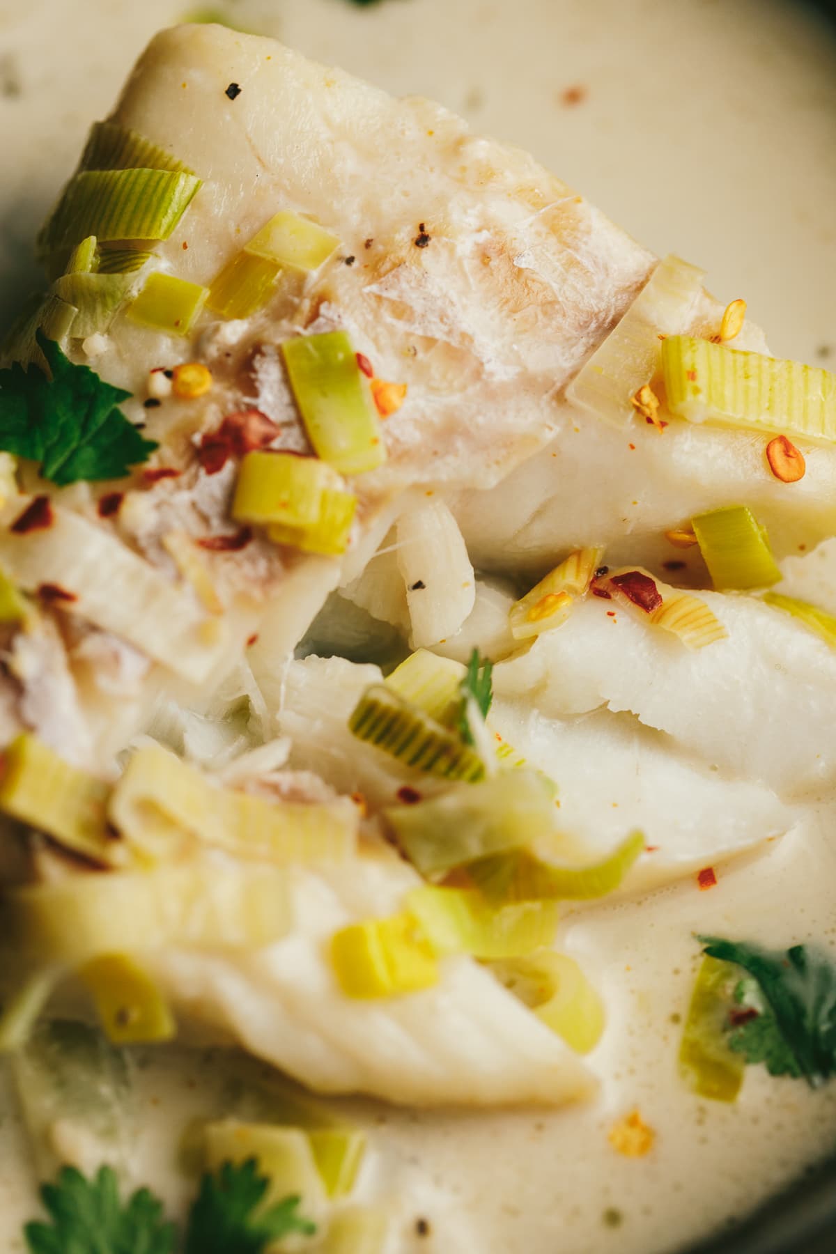 Flaky cod poached in coconut milk with garnishes on top.