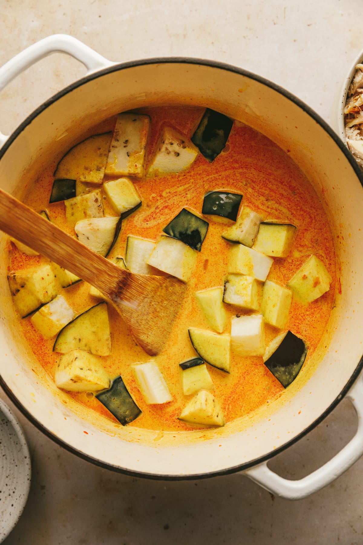 A large pot of keto red curry with cubed eggplant and a wooden spoon.