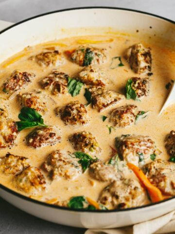 Keto turkey meatballs in a creamy red curry sauce with a spoon.
