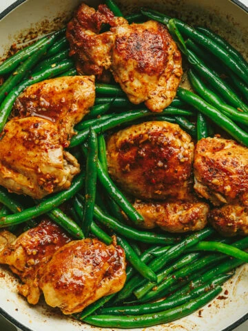 An overhead image of a braiser with cooked chicken thighs, green beans and a lemon garlic butter sauce.