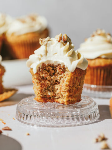 A keto carrot cake cupcake on a glass dish with other cupcakes in the background.