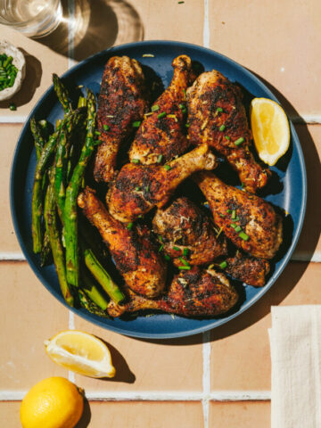 A plate of pan-fried chicken legs with zaatar seasoning and a side of asparagus.