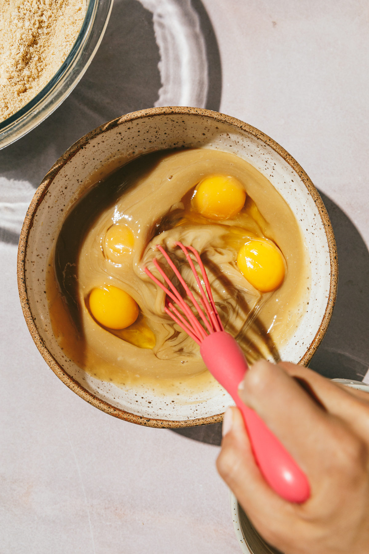 Whisking wet ingredients and eggs in a bowl with a pink whisk.