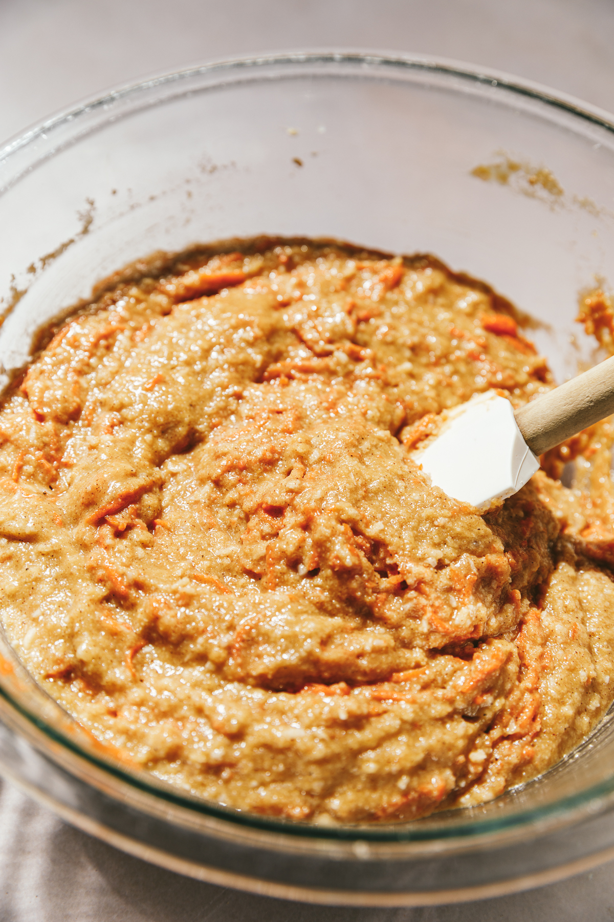 Carrot cake batter with in a glass bowl with a white spatula.