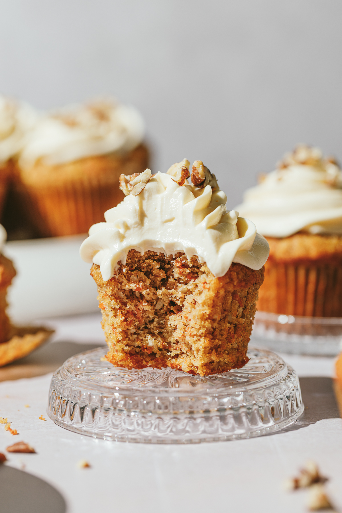 A keto carrot cake cupcake on a glass dish with other cupcakes in the background.