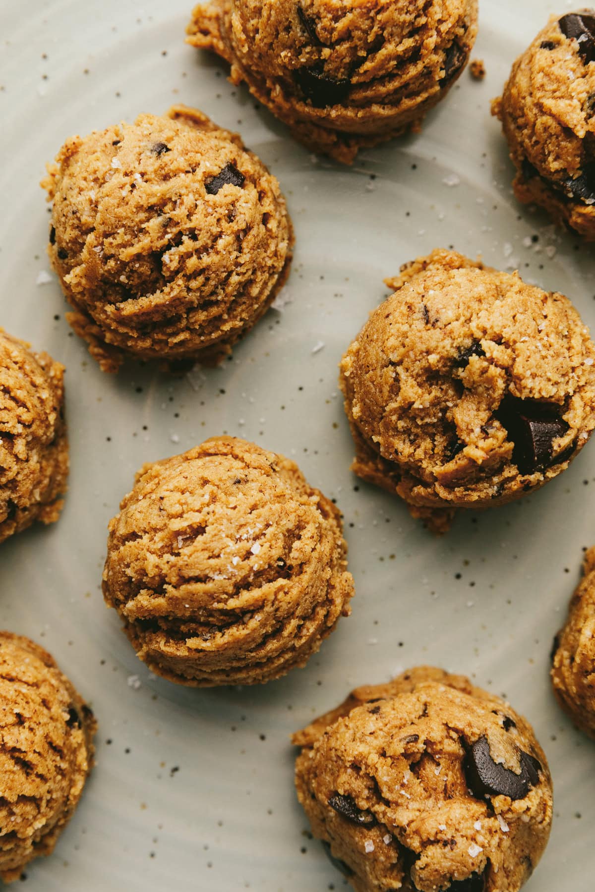 Several cookie dough protein balls on a serving plate with sea salt flakes.