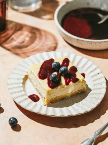 A small plate with a slice of keto lemon ricotta cheesecake and a mixed berry sauce behind it.