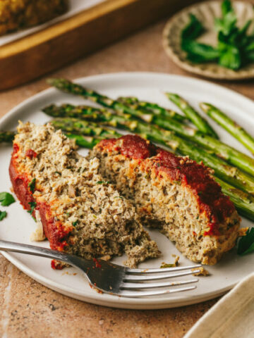 Two slices of keto turkey meatloaf on a plate with roasted asparagus.
