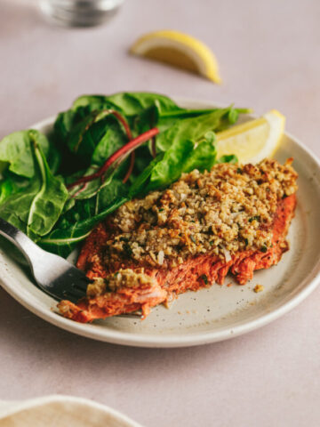 A plate of pecan coconut crusted salmon with lemon wedges and salad.