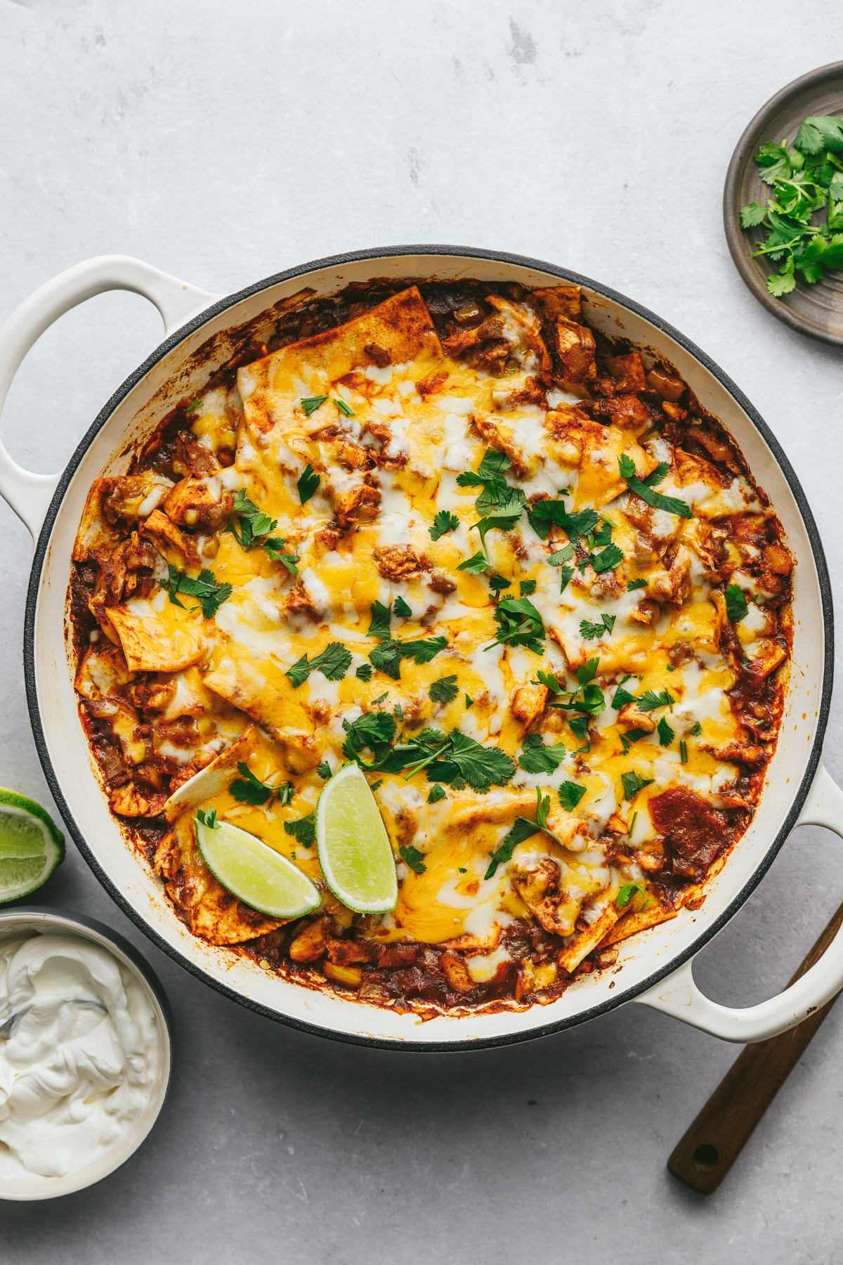 Overhead image of a baked keto chicken enchilada skillet with cilantro and fresh lime wedges on top.