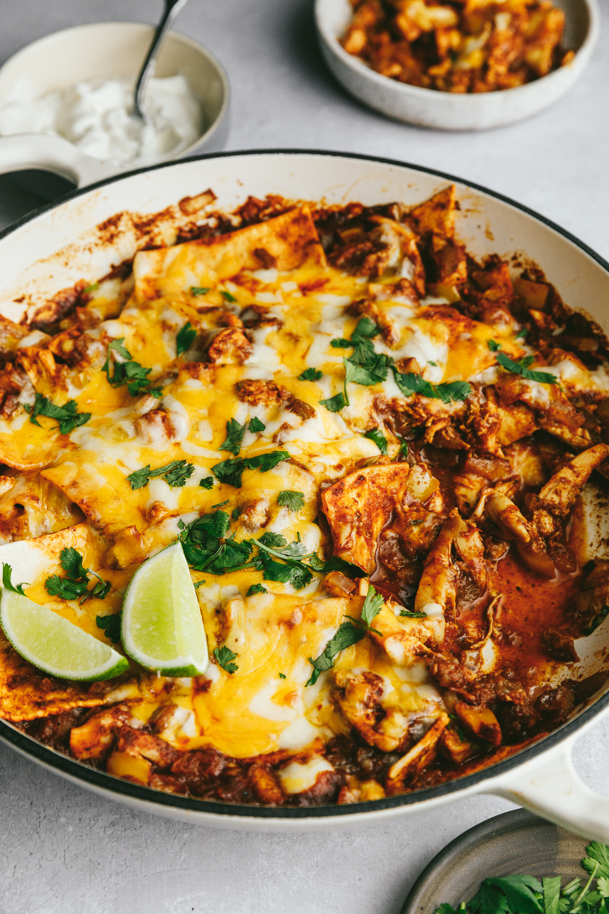 A low-carb chicken enchilada casserole in a large braiser dish with toppings around it.