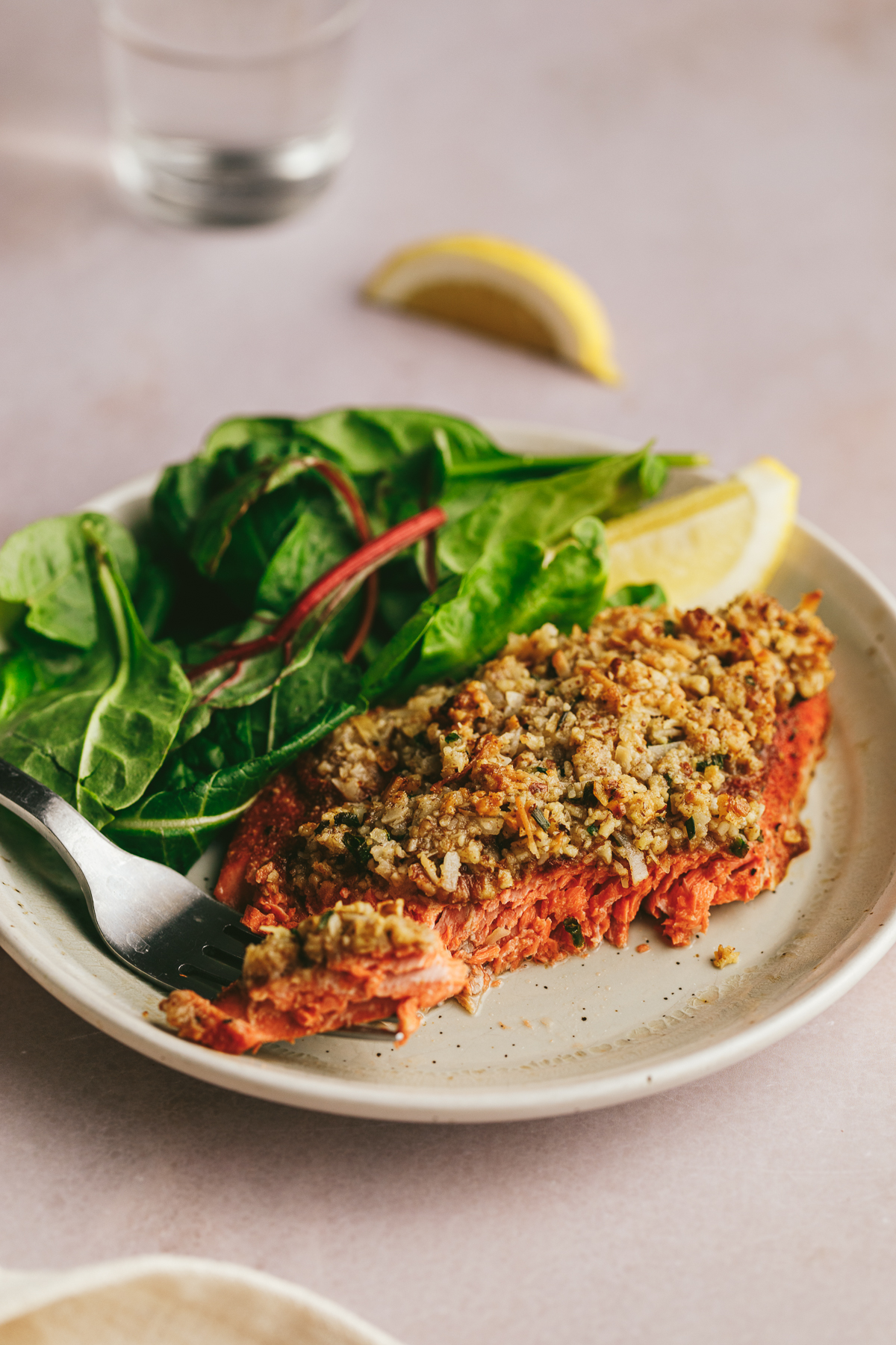 A plate of pecan coconut crusted salmon with lemon wedges and salad.