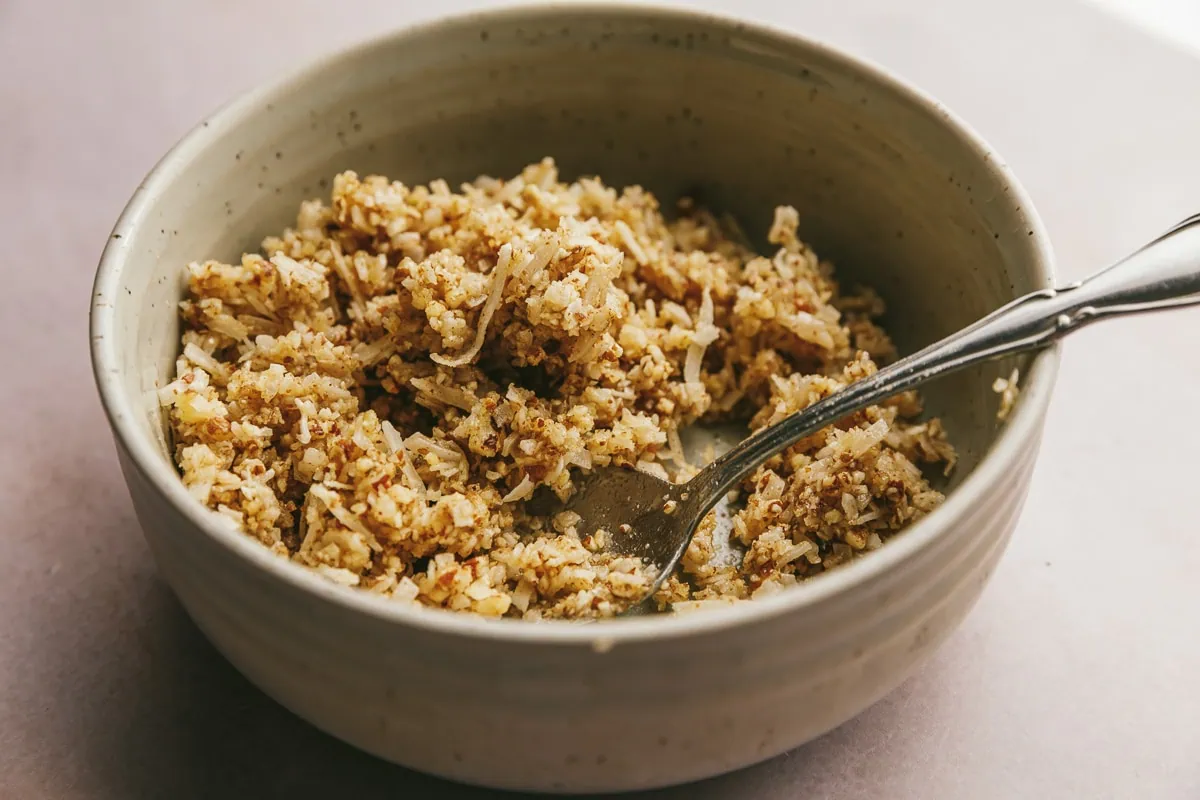 Pecan and coconut mixture in a small bowl with a spoon.