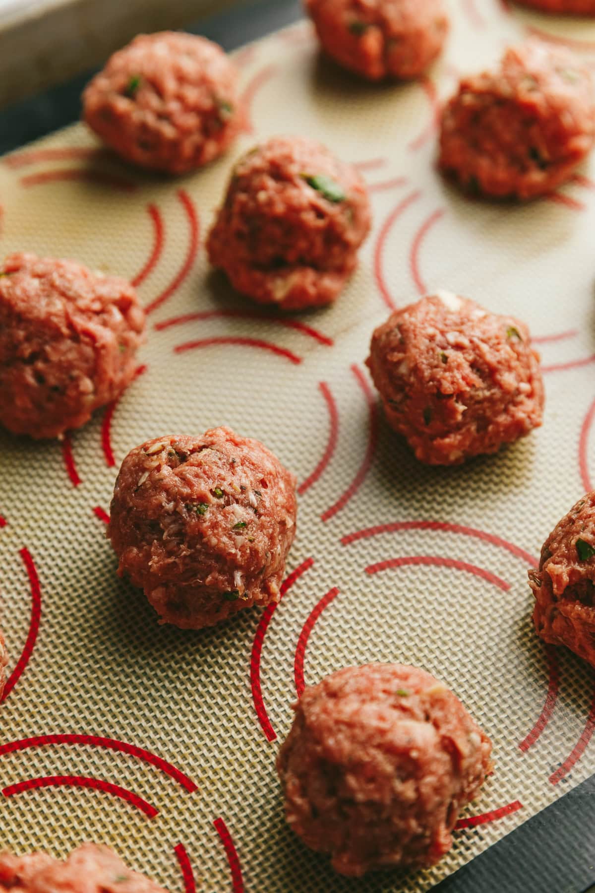 Raw meatballs on a baking sheet with a silpat baking mat.