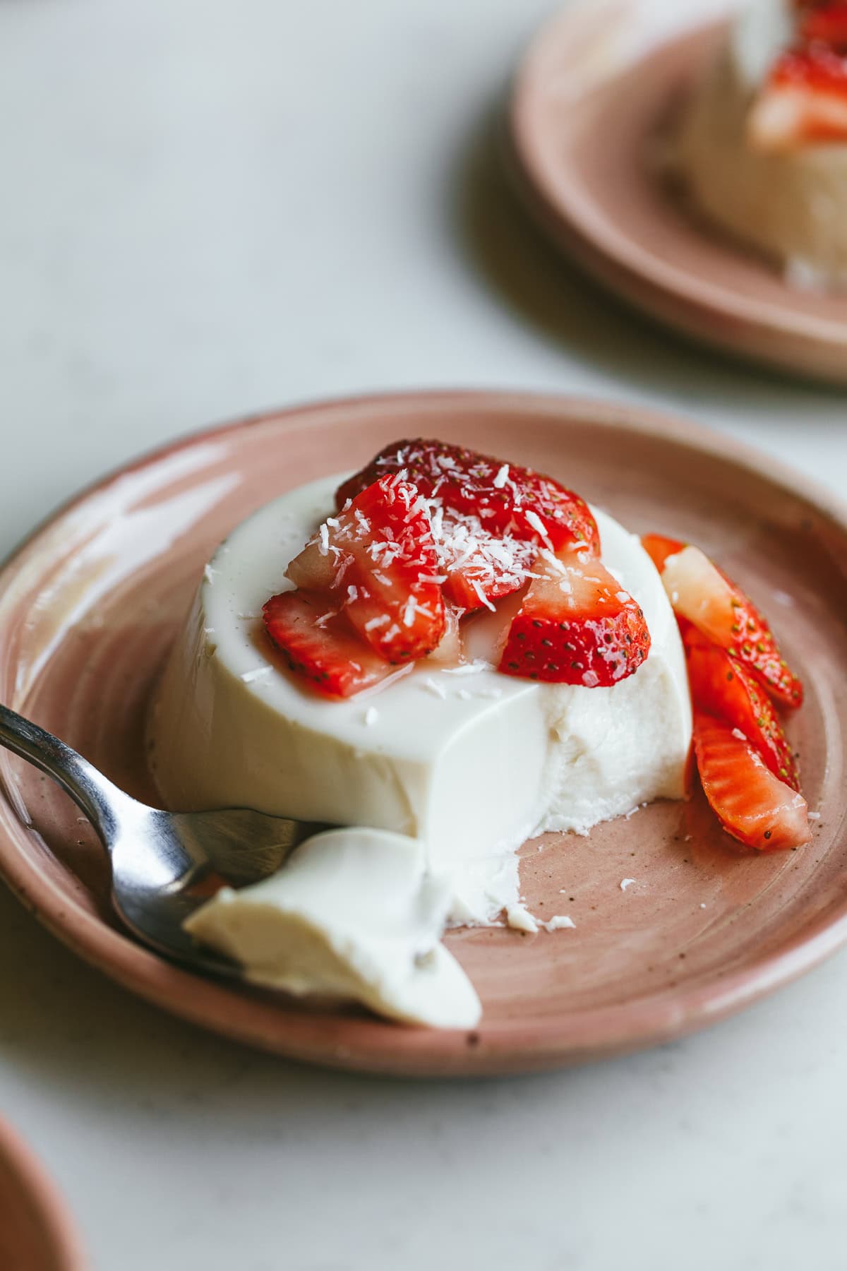 Coconut panna cotta with strawberries and shredded coconut on top, sitting on a pink dessert plate.