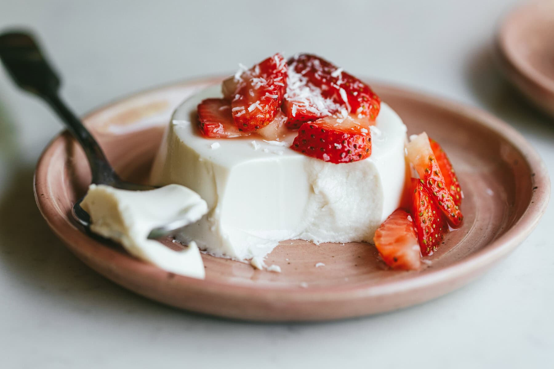 Closeup of coconut panna cotta on a pink dessert plate with strawberries.