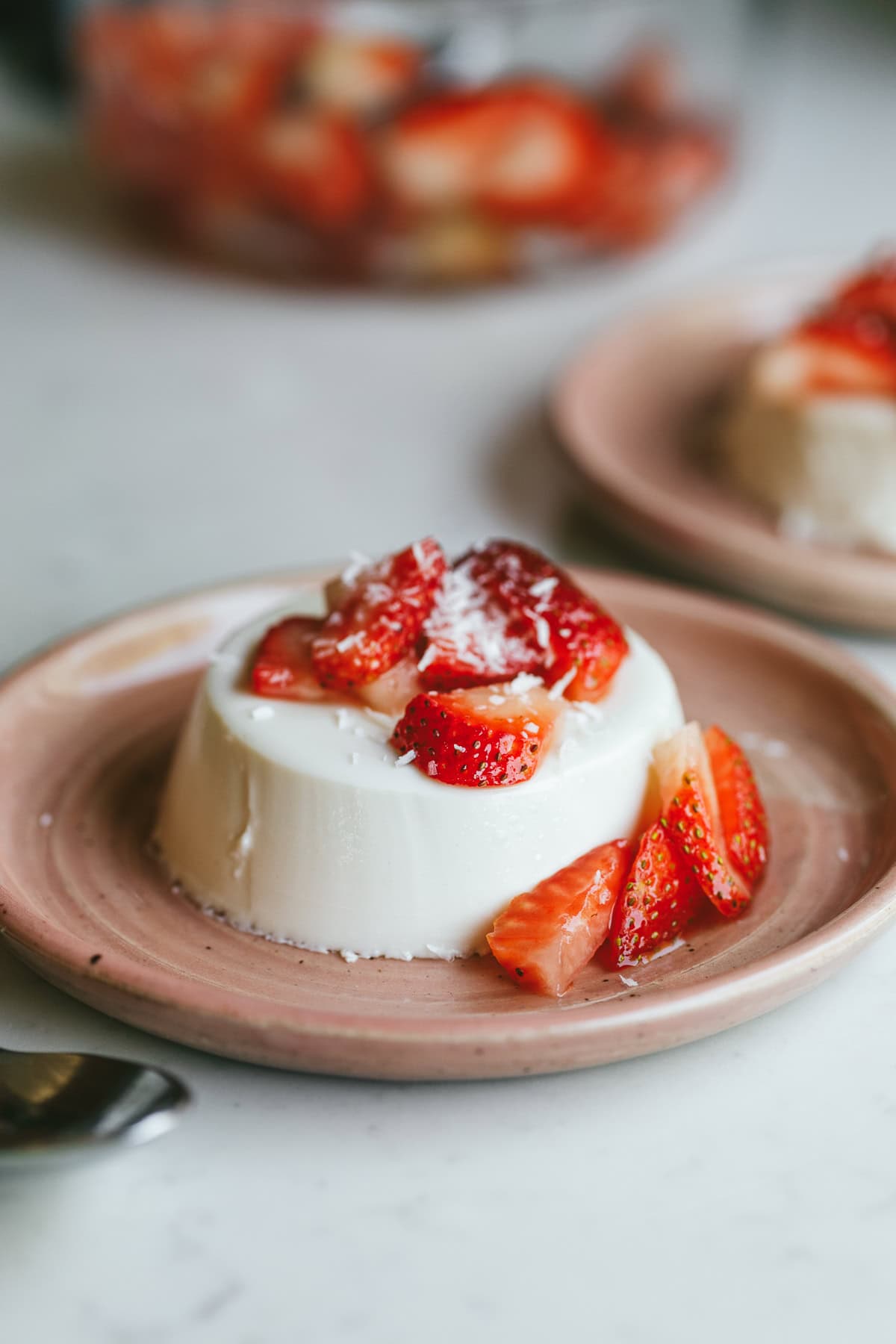 Coconut panna cotta served on a pink dessert plate topped with strawberries.