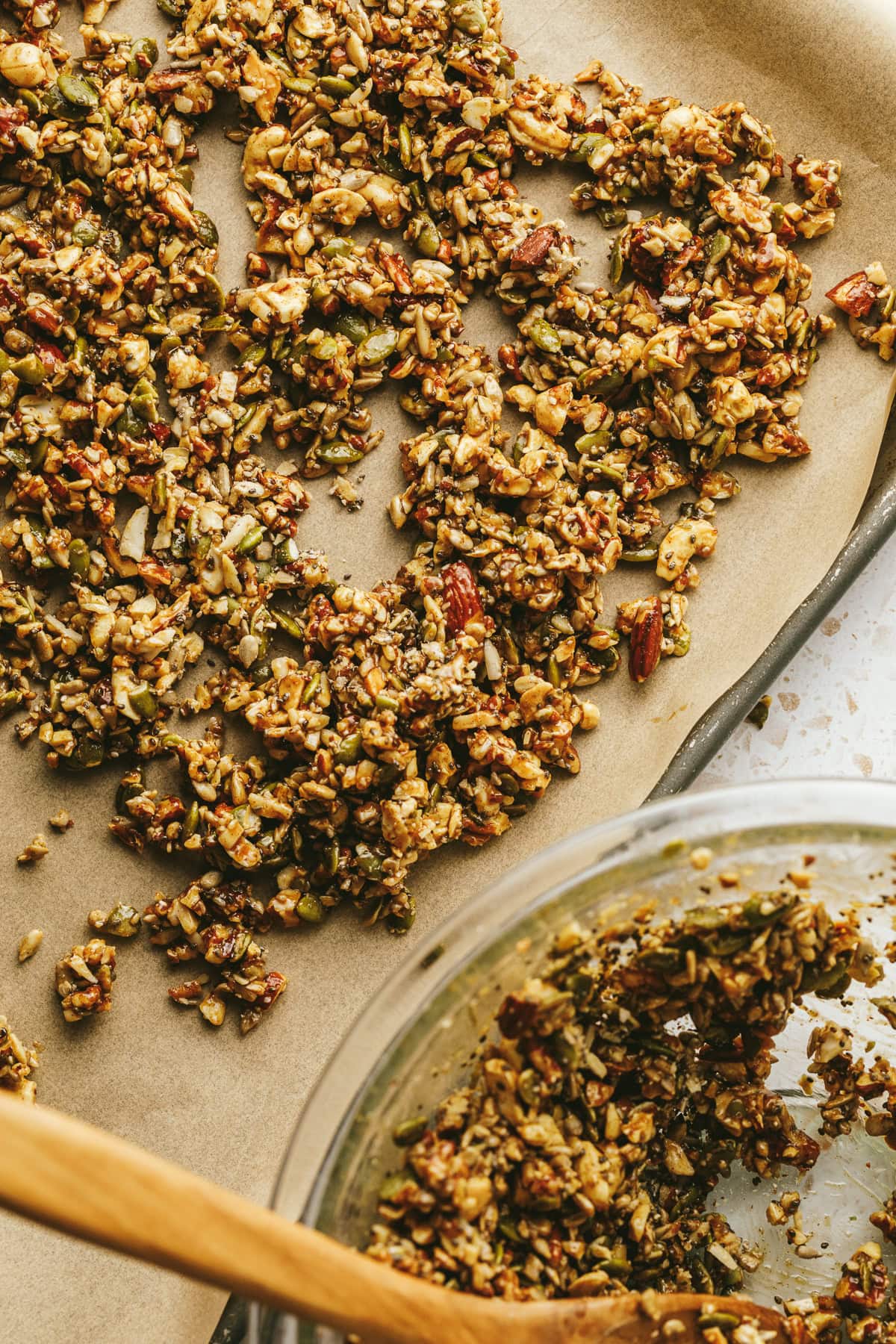A bowl with the vanilla almond butter granola next to a baking sheet with the mixture being spread on top.