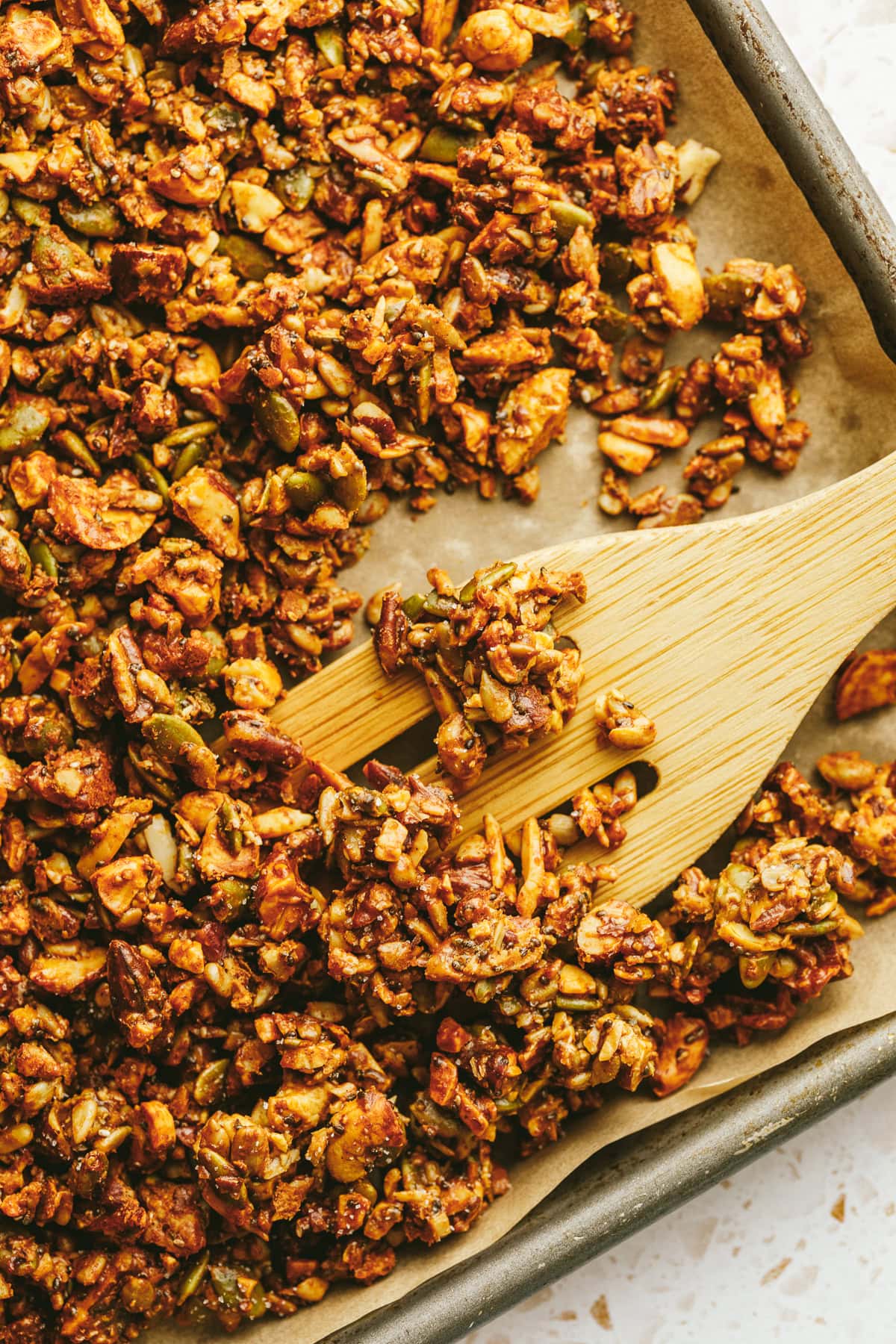 A sheet pan of golden brown grain-free granola and a wooden spatula.