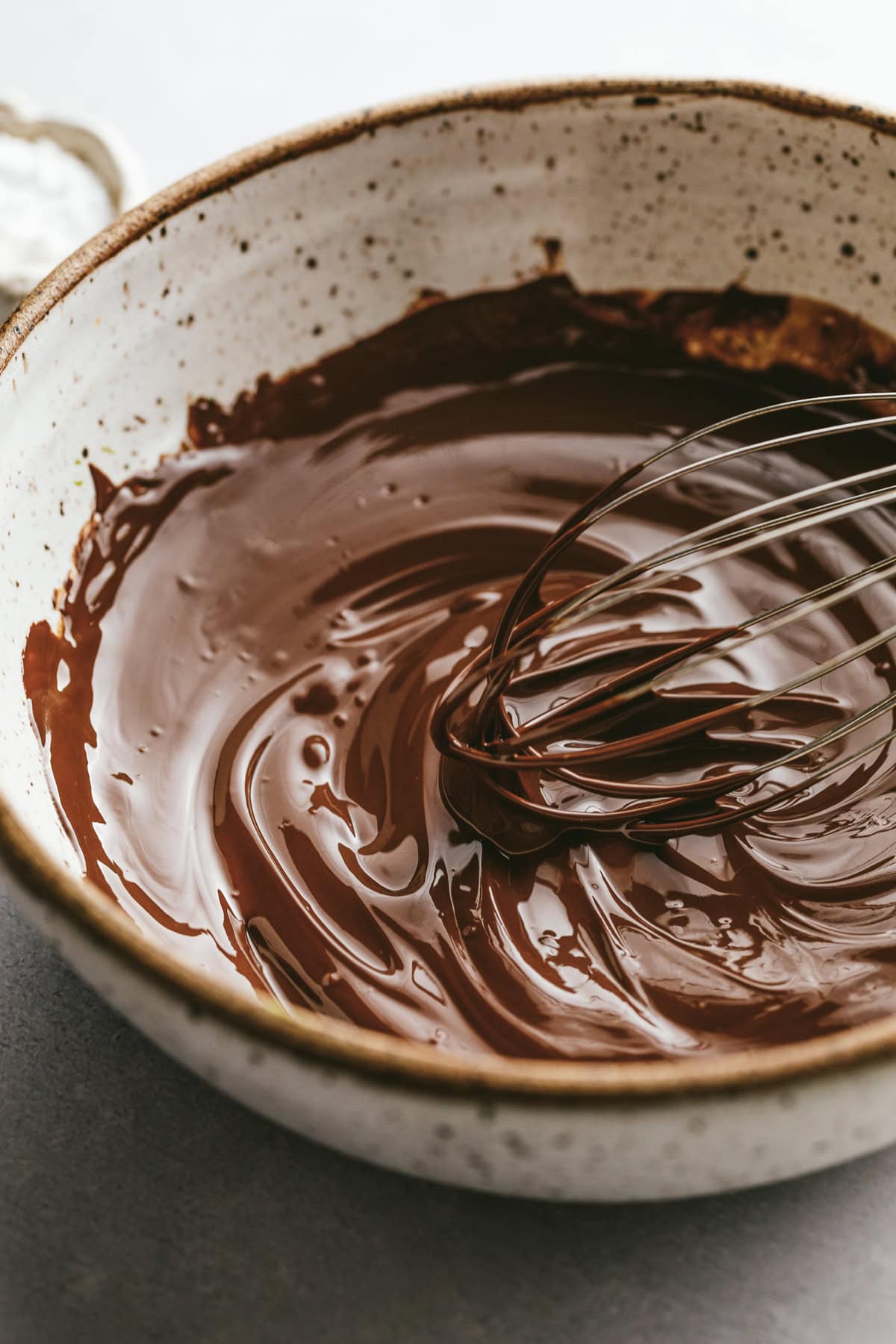 A whisk in a bowl of melted dark chocolate.