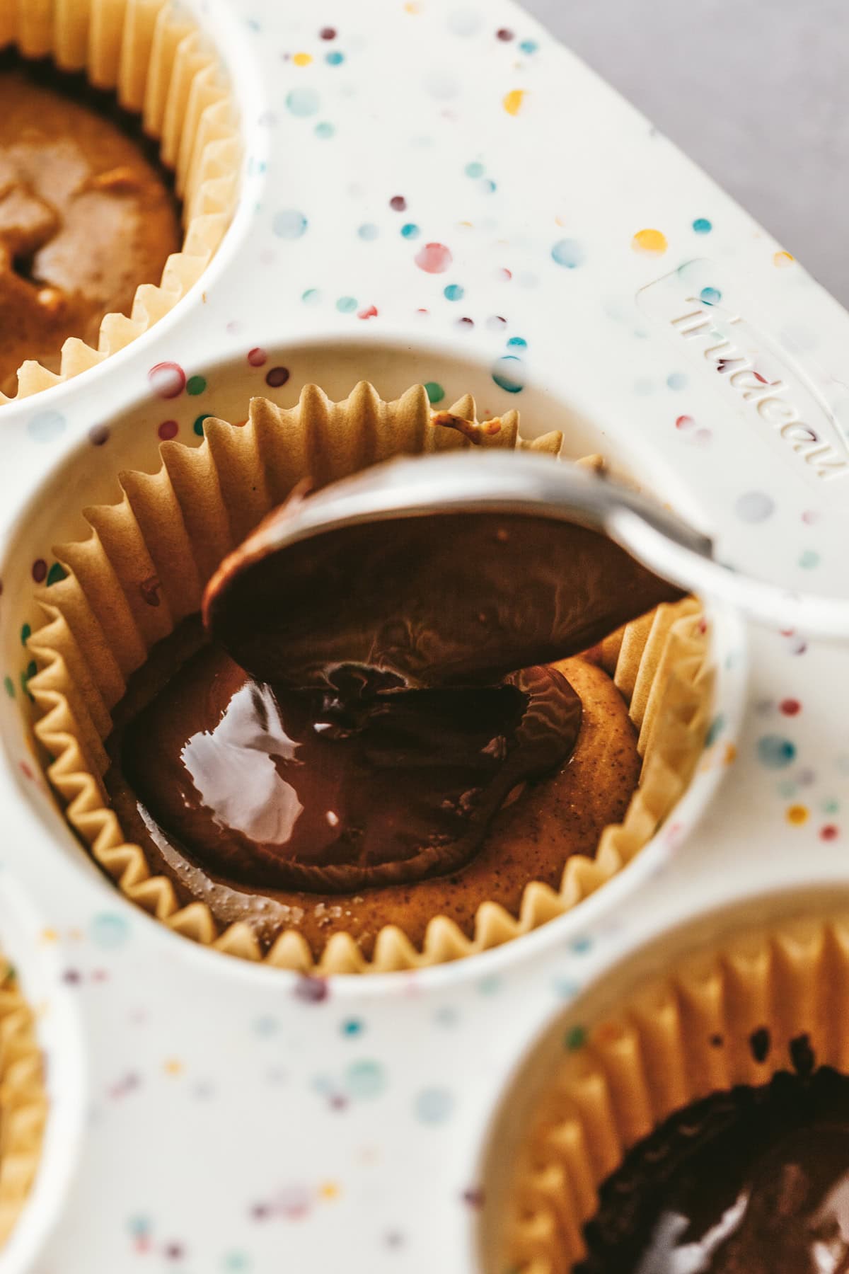 Spooning chocolate on top of almond butter cups.