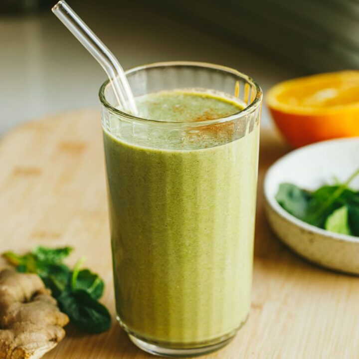 A serving of green ginger smoothie in a glass with a straw.