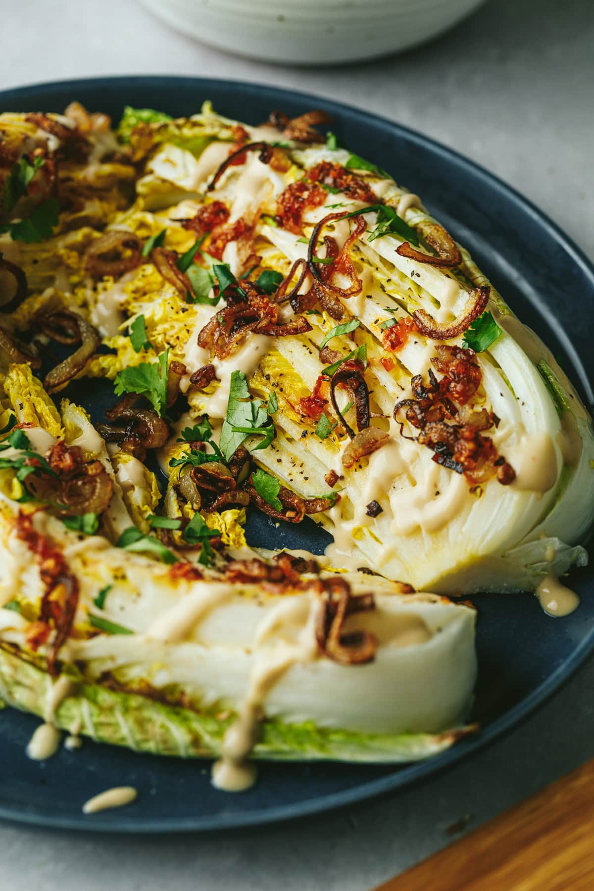 A blue plate with roasted napa cabbage and toppings.