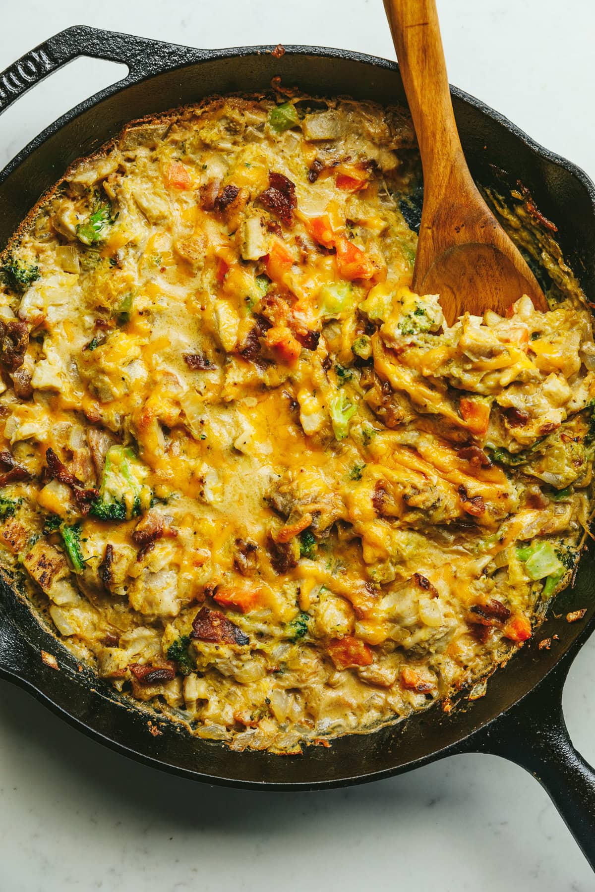 A baked alfredo chicken and broccoli casserole with a wooden spoon.