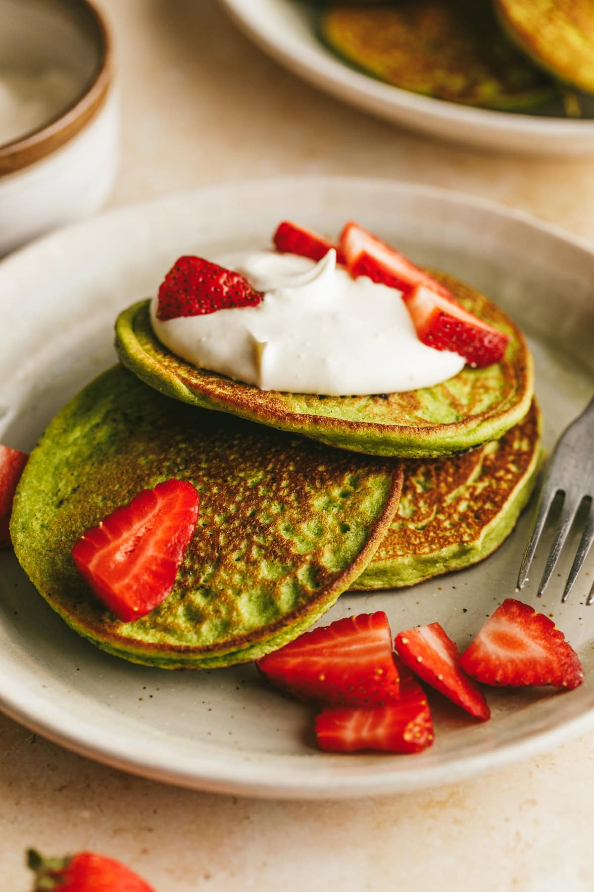Closeup of a stack of banana spinach pancakes with strawberries and whipped cream.
