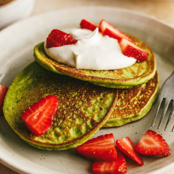 Three banana spinach pancakes on a serving plate with a fork.