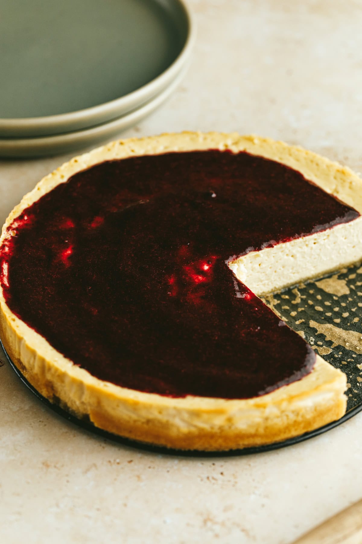 A high protein cheesecake with berry sauce and plates stacked.